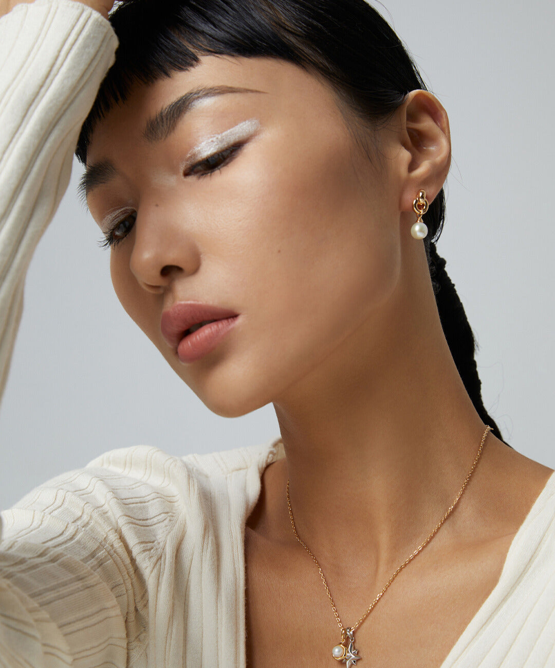 A woman wearing a white sweater and earrings, showcasing gold plated pearl earrings and a matching necklace.