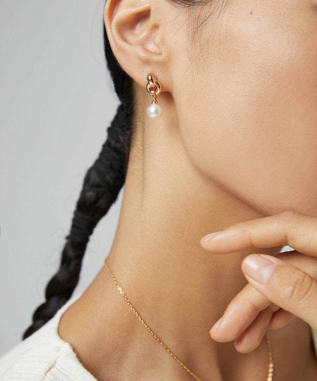 Woman with gold interlocked knot pearl earring and gold chain necklace.