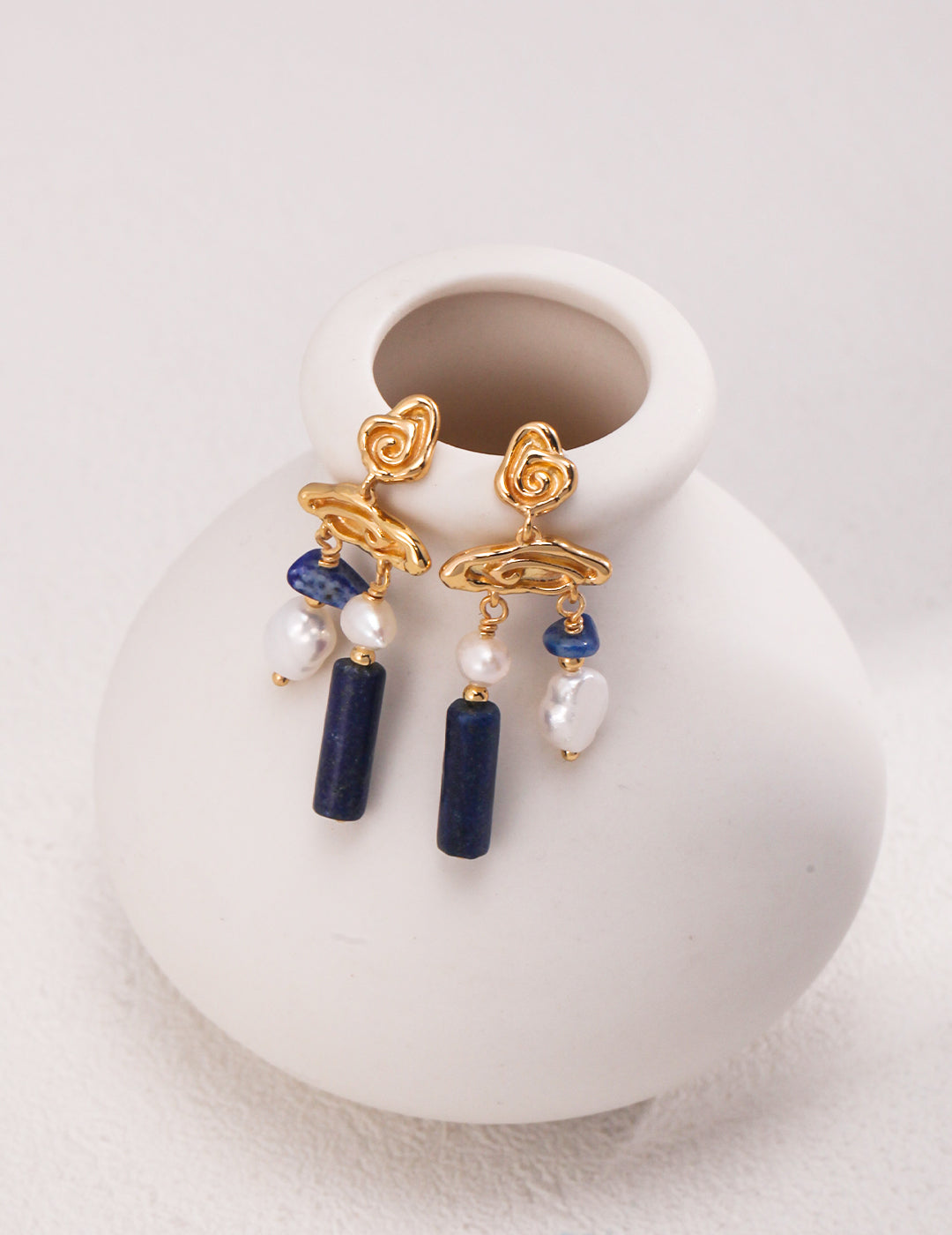 Gold plated dangles with lapis lazuli and freshwater pearls hanging on white vase.