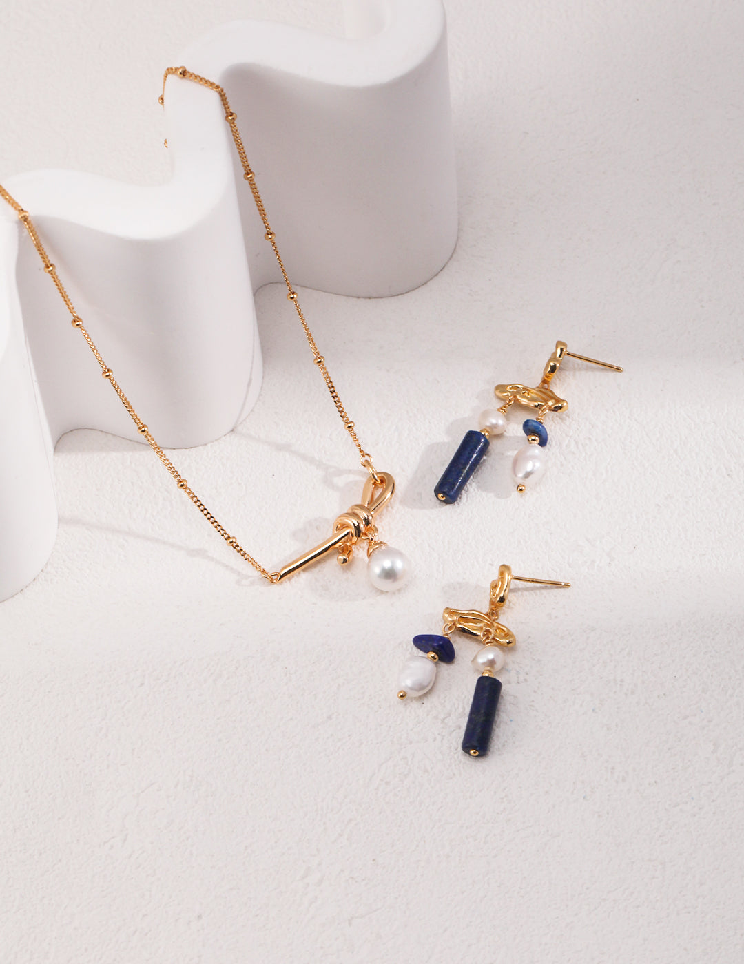 Elegant gold jewelry set featuring blue lapis lazuli stones and freshwater pearls, with a pearl necklace.