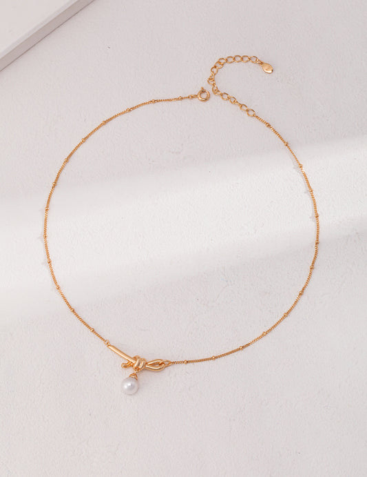 Elegant gold necklace with pearl knot charm.