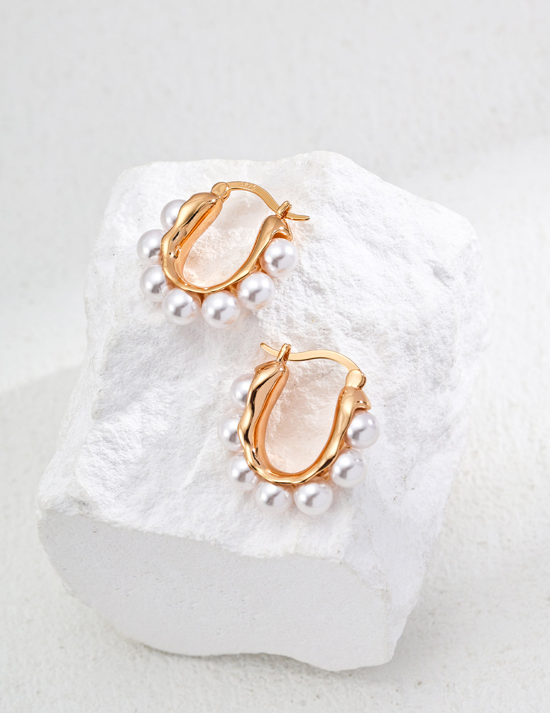 A pair of gold hoop earrings featuring shell pearls, beautifully displayed on a white rock surface.