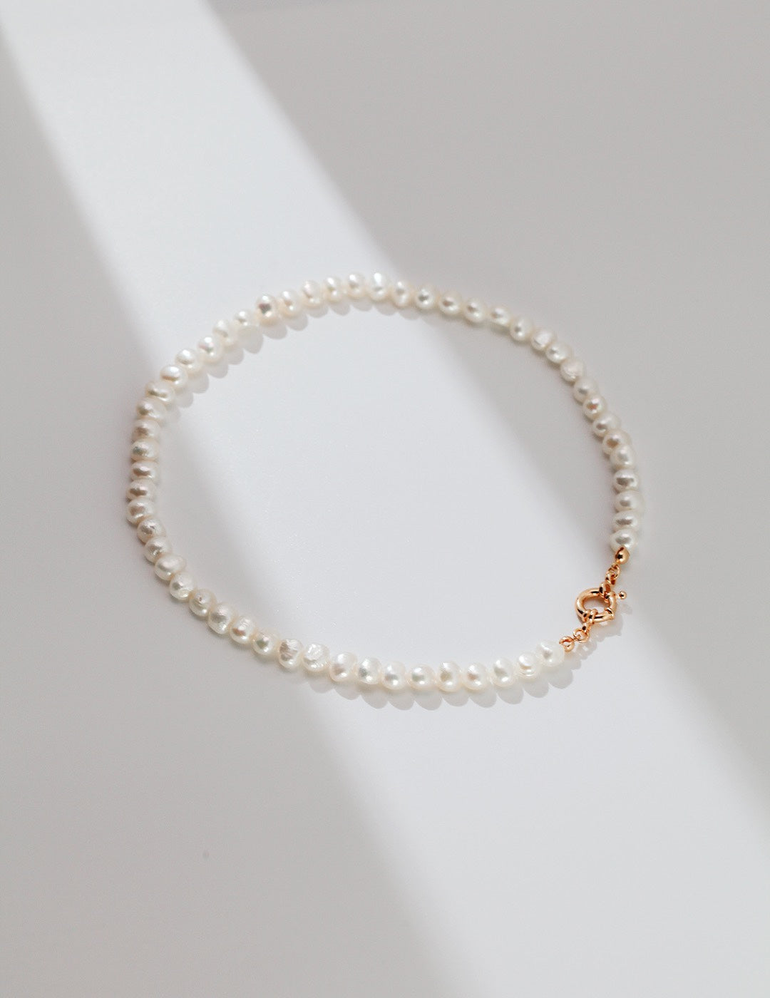 Top-down view of the Miley Necklace on a white backdrop, focusing on the gold clasp detail and pearl spacing.