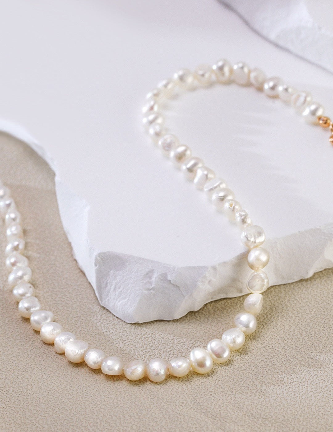 The Miley Necklace curved gracefully on textured stone, highlighting the contrast between the organic white pearls and the gold clasp.