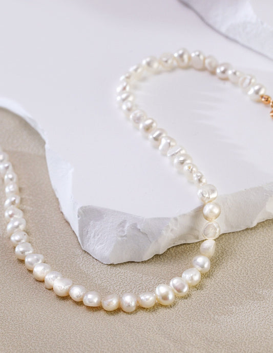 The Miley Necklace curved gracefully on textured stone, highlighting the contrast between the organic white pearls and the gold clasp.