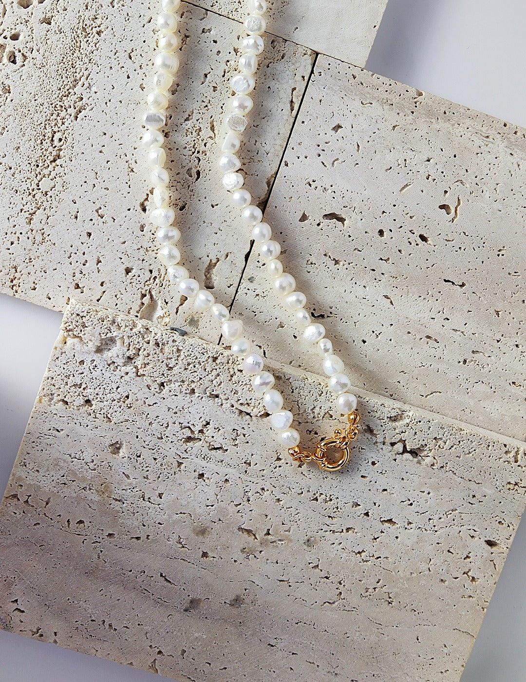 A close-up detail of the Miley Necklace’s polished gold circular clasp, showing the intricate hand-strung freshwater pearls.