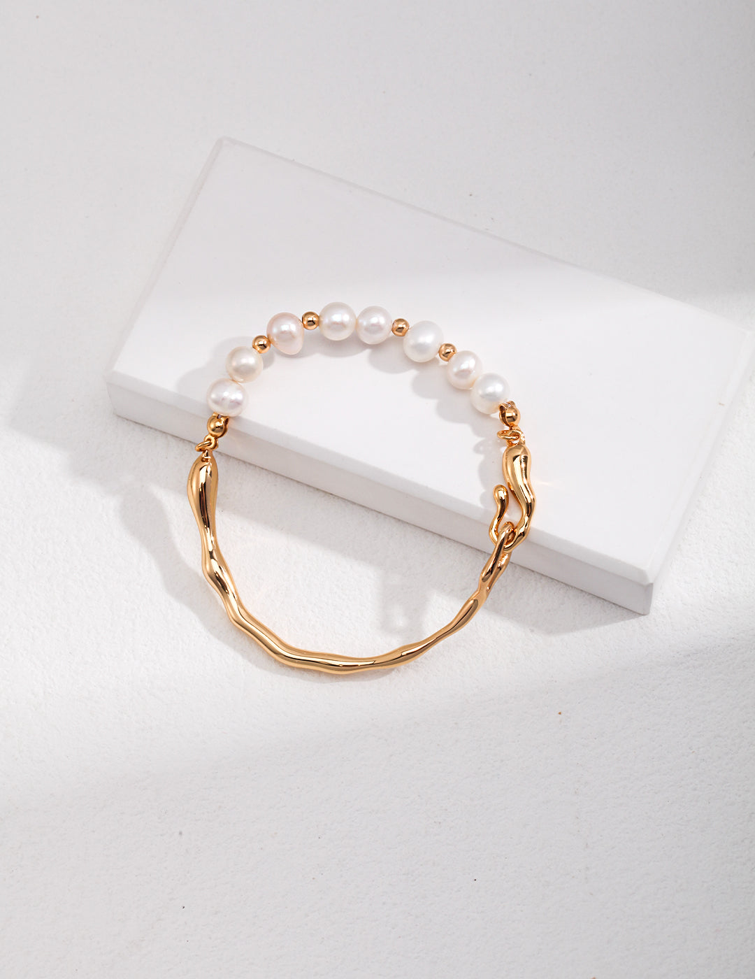 A half gold plated bangle adorned with freshwater pearls, presented in a white box.