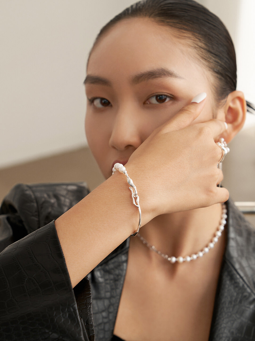 A woman wearing a silver bangle and freshwater pearls bracelet, complemented by a necklace.