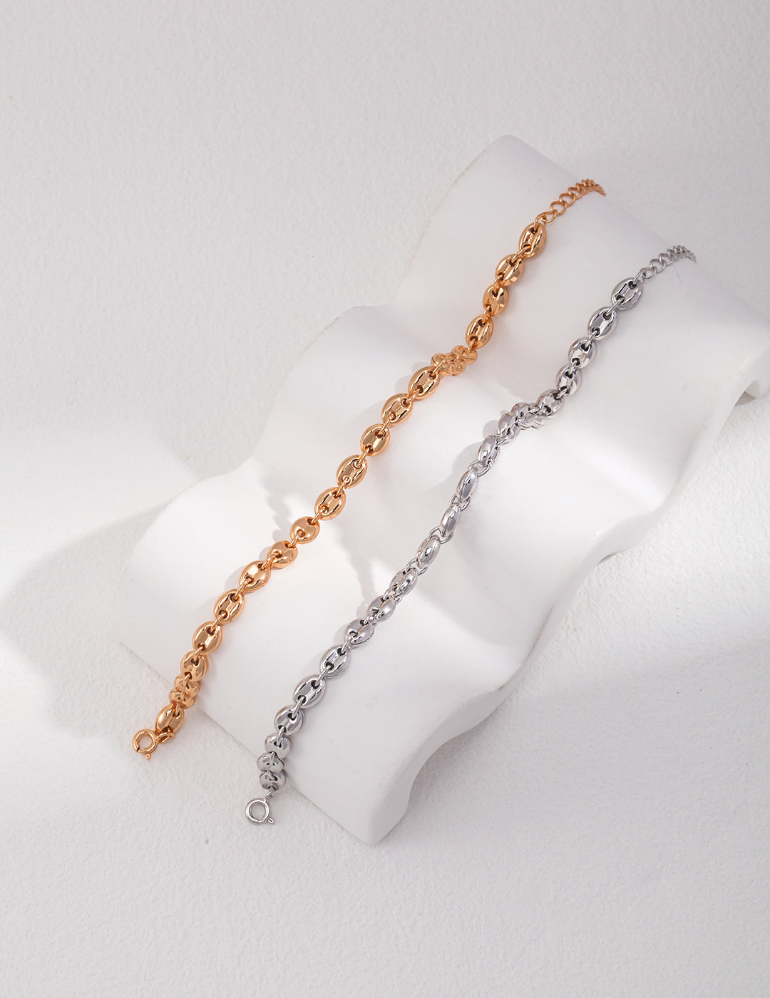 Two interlocking link bracelets in gold and silver on a white surface.