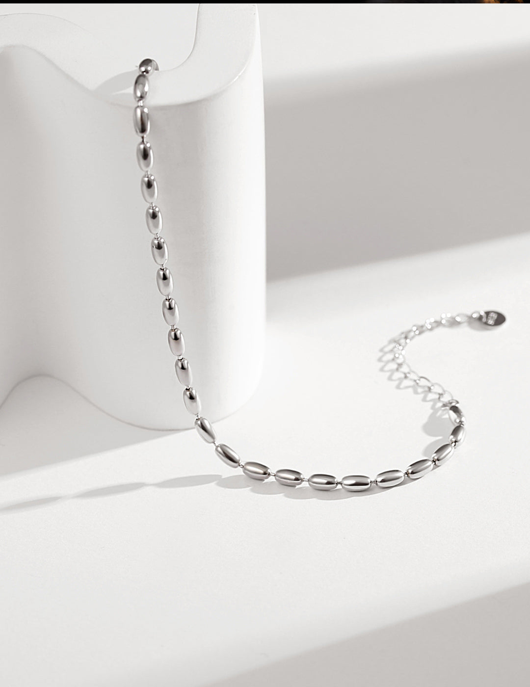 A delicate silver chain bracelet with silver plated dainty beads, resting on a pristine white surface.