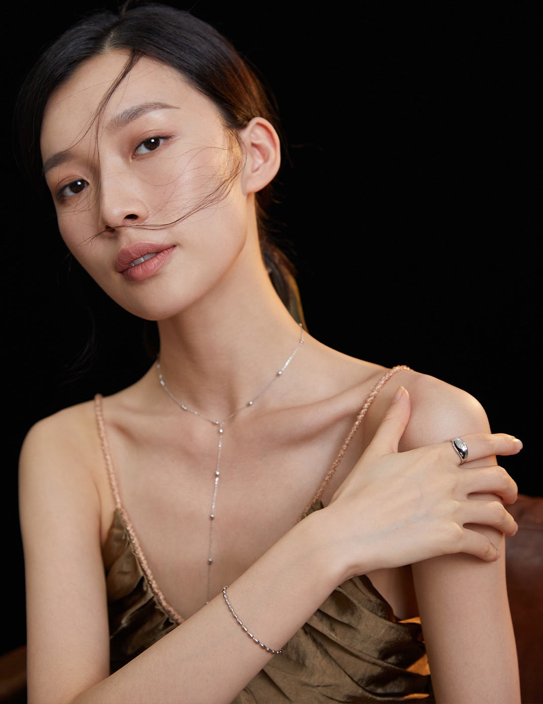 A woman in a gold dress poses for a photo, accessorized with a silver plated dainty beads bracelet and other jewelry.