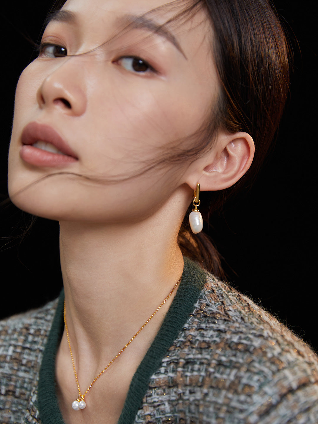 A stunning model wearing a gold plated necklace, complemented by baroque pearl hoop earrings.