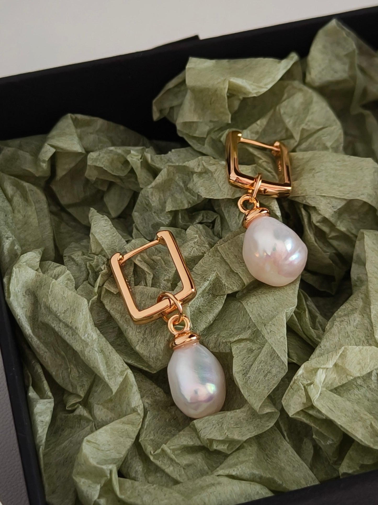 Gold hoop earrings with white baroque pearls in a box.