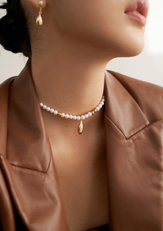 An elegant woman donning a gold necklace and pearl choker, radiating timeless beauty.