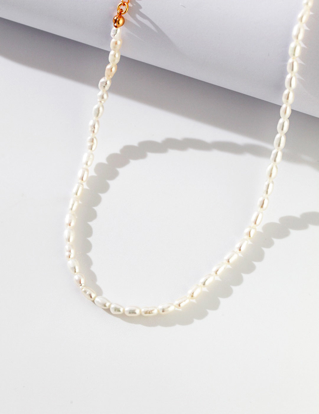 Dainty rice pearl necklace from Mezuille on white surface with a soft shadow