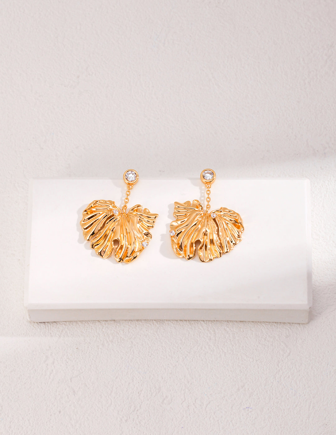 Gold leaf earrings on a white surface, featuring delicate dangles resembling leaves.