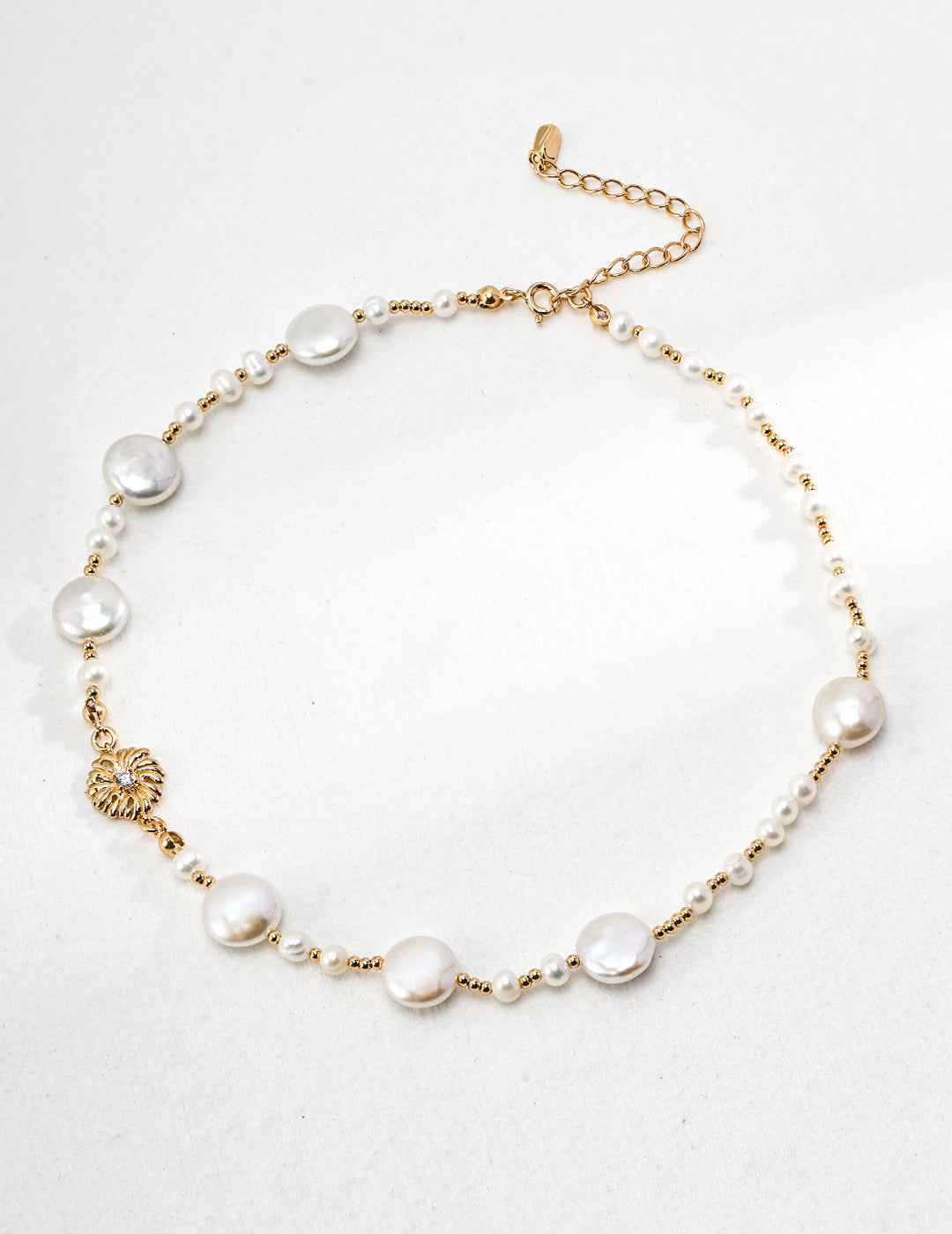 Gold necklace with dainty beads and freshwater pearls in irregular sizes, featuring a charming pendant.