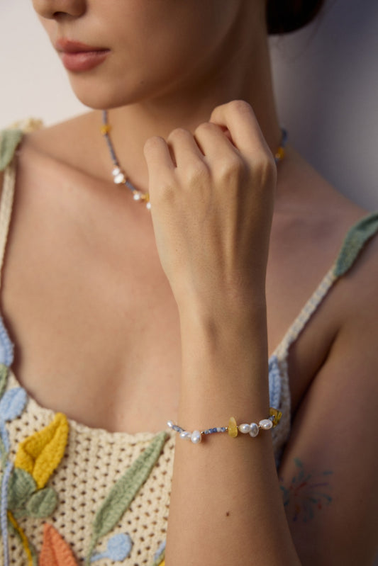 A woman showcases a yellow and blue bracelet crafted from Azurite in Granite, beeswax, and freshwater pearls.