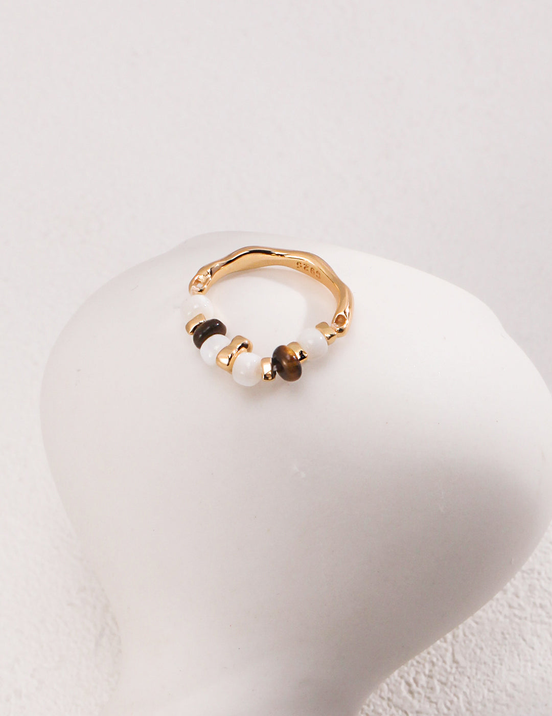 A stunning gold ring adorned with white beads, featuring shell beads and tiger's eye accents.