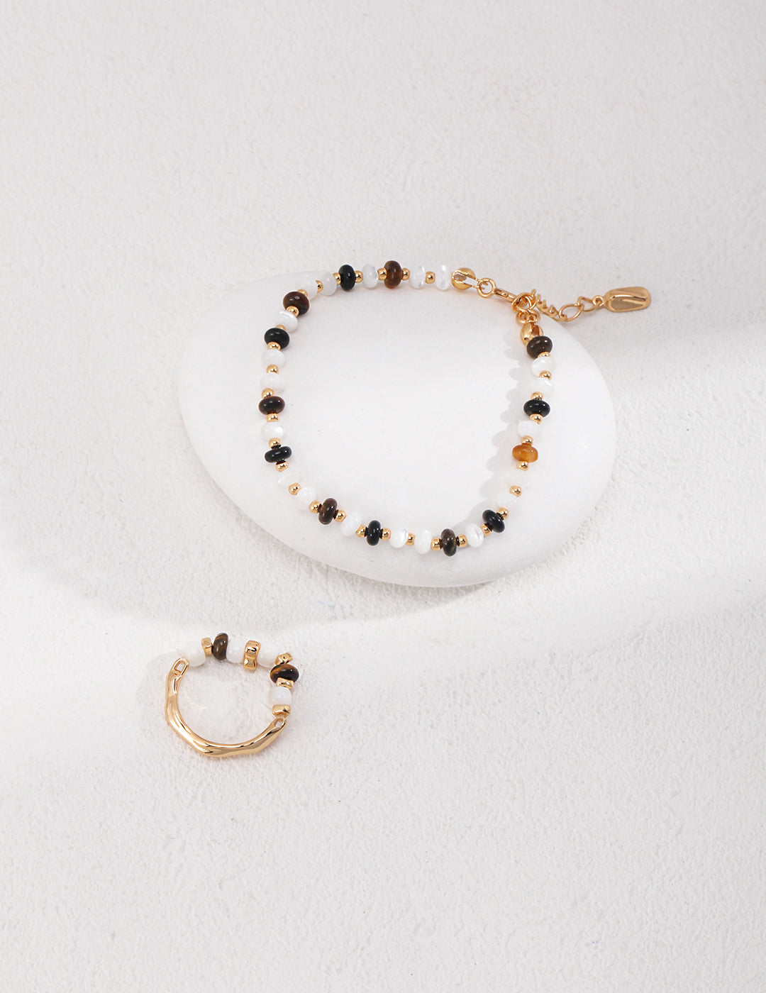 Elegant gold ring and bracelet set with shell beads and tiger's eye on white background.