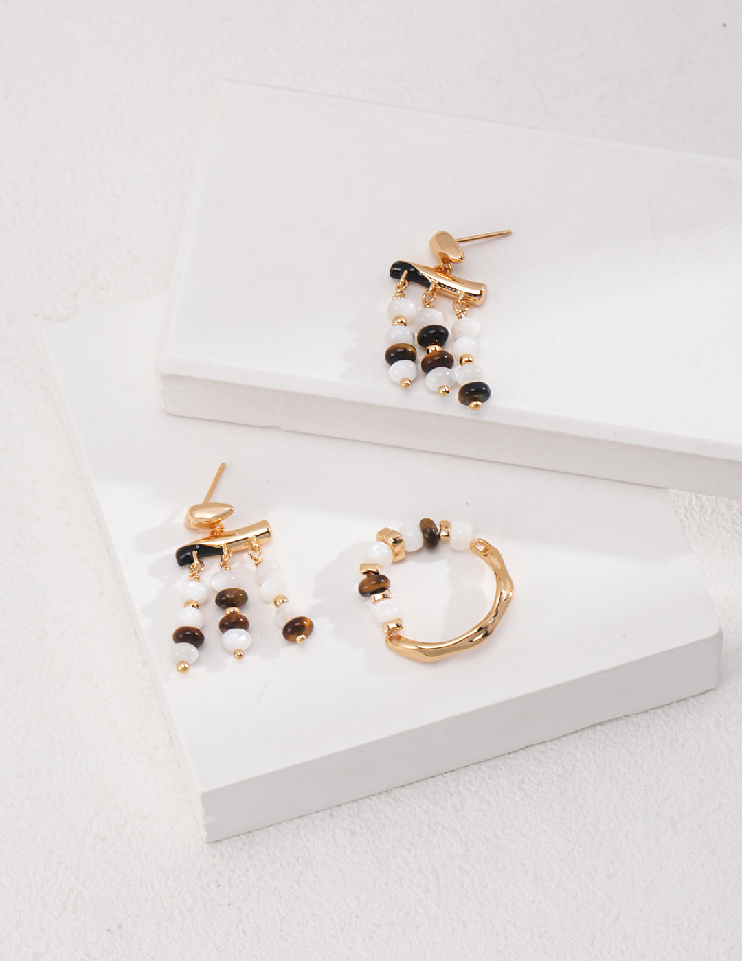 A pair of earrings with black and white beads, along with a gold ring adorned with shell beads and tiger's eye.