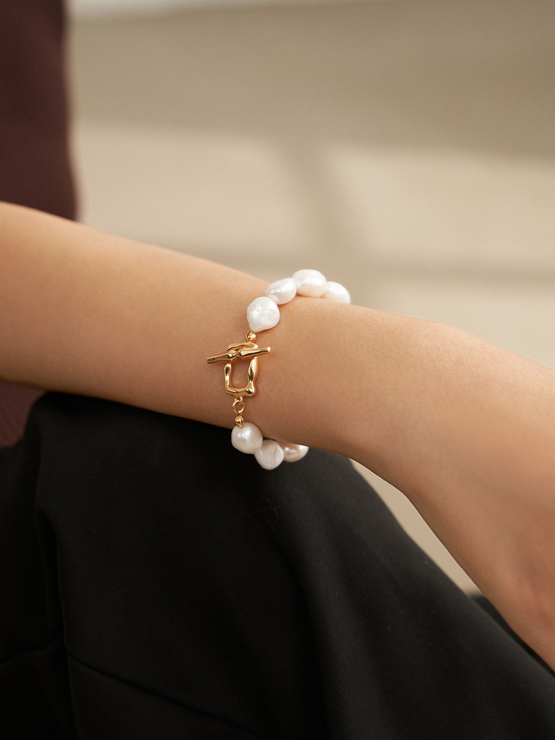 Woman wearing white baroque pearl bracelet with gold chain and clasp on wrist.