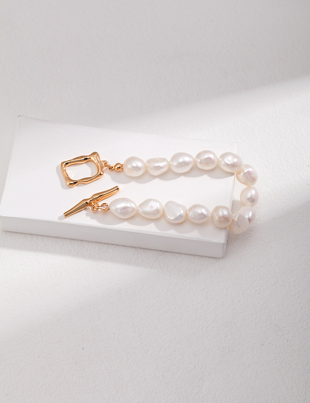 Stylish white pearl bracelet featuring a luxurious gold toggle clasp.