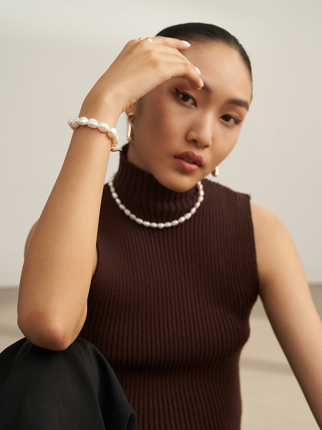 A stylish woman in a brown turtle neck top and pearl bracelet exudes elegance and sophistication.