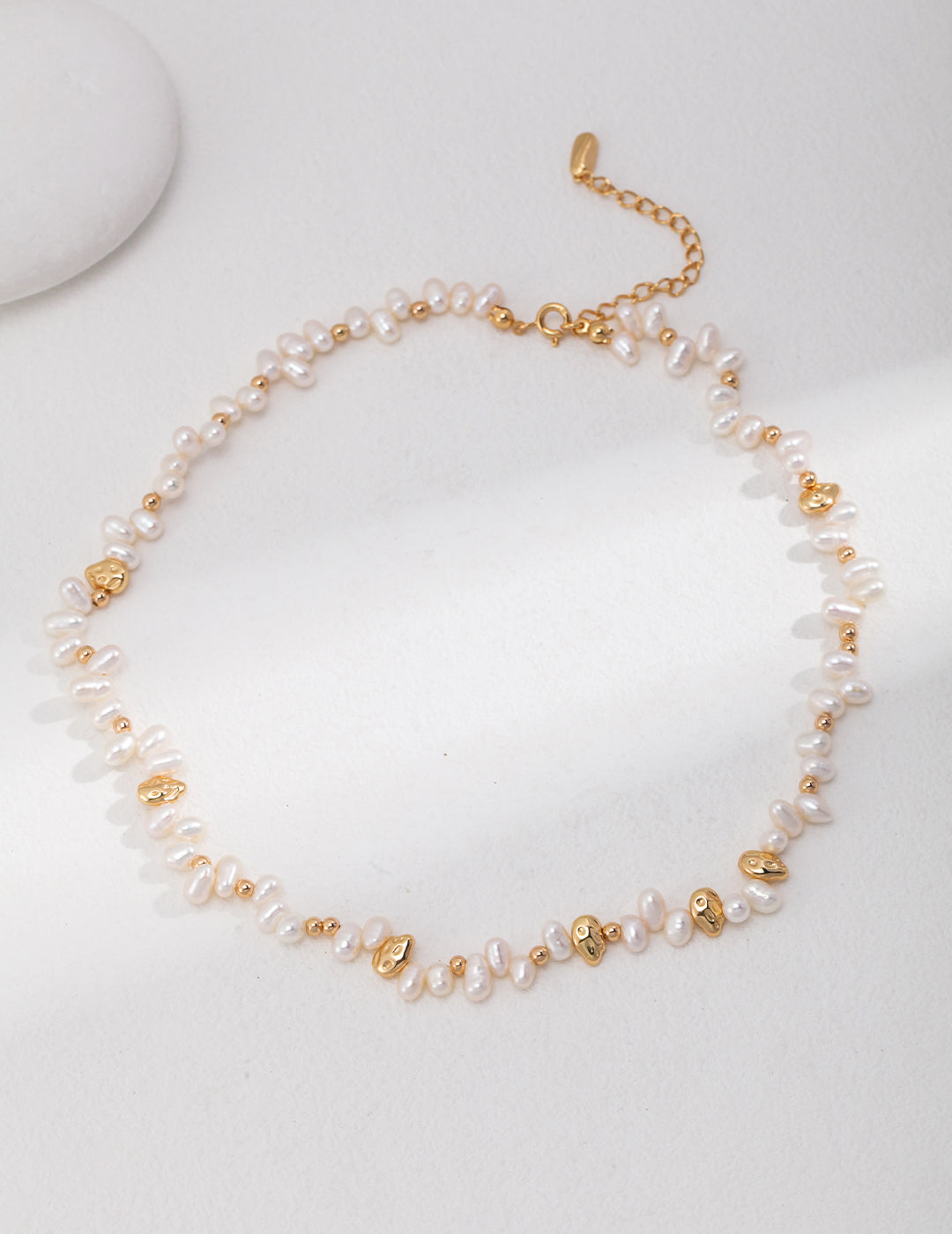 Elegant gold and white pearl necklace on white background.