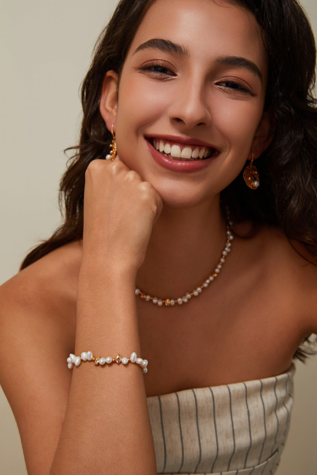 Editorial lifestyle photograph of a smiling model wearing the Natasha gold pearl necklace and matching bracelet stack, showcasing how the pieces catch the light for an elegant look.