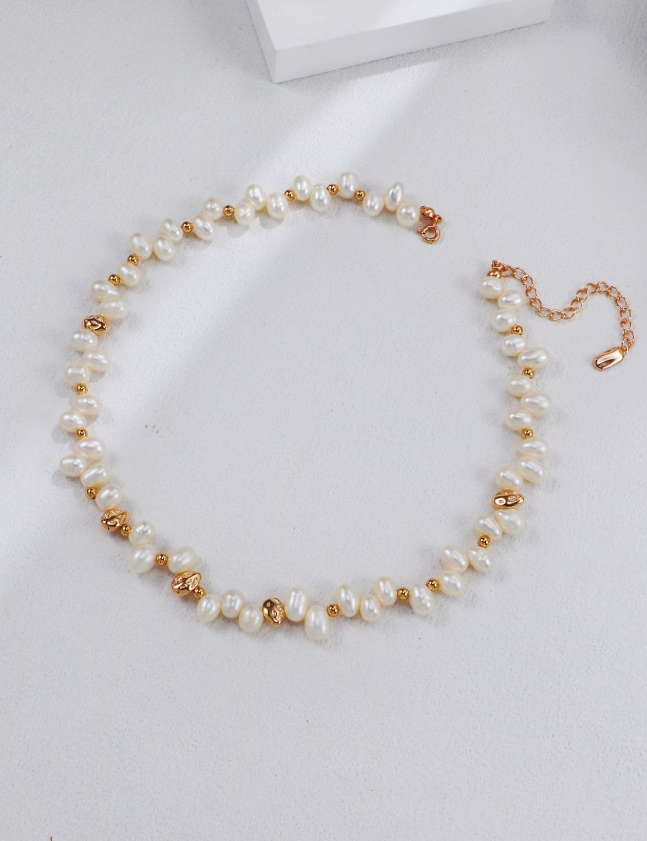 Studio product photograph of the Natasha necklace laid out in a full circle. Features a continuous strand of delicate white freshwater pearls accented by organic, molten-textured gold nuggets.