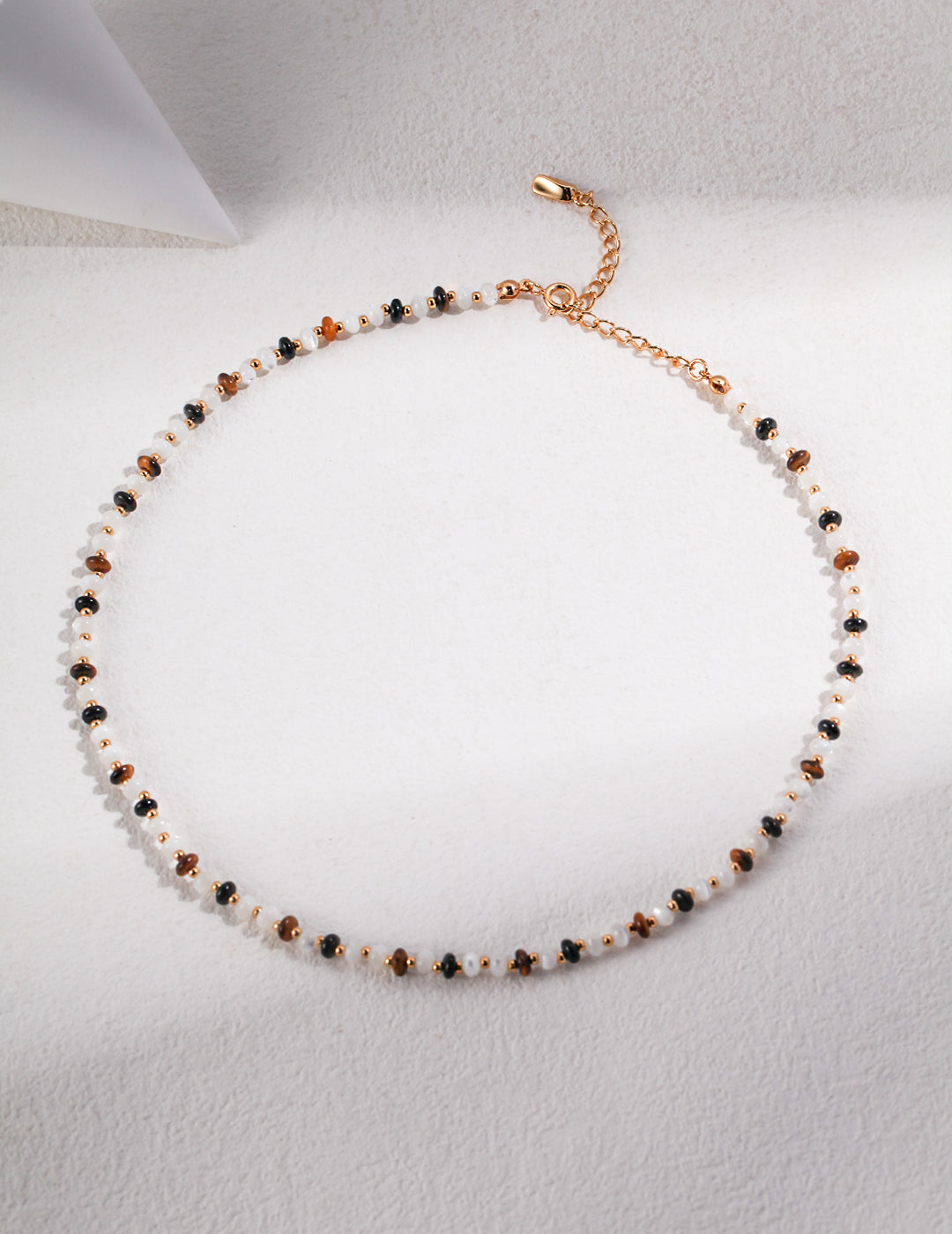 A stunning necklace adorned with gold plated and white silk beads, black agate, and tiger's eye stones.