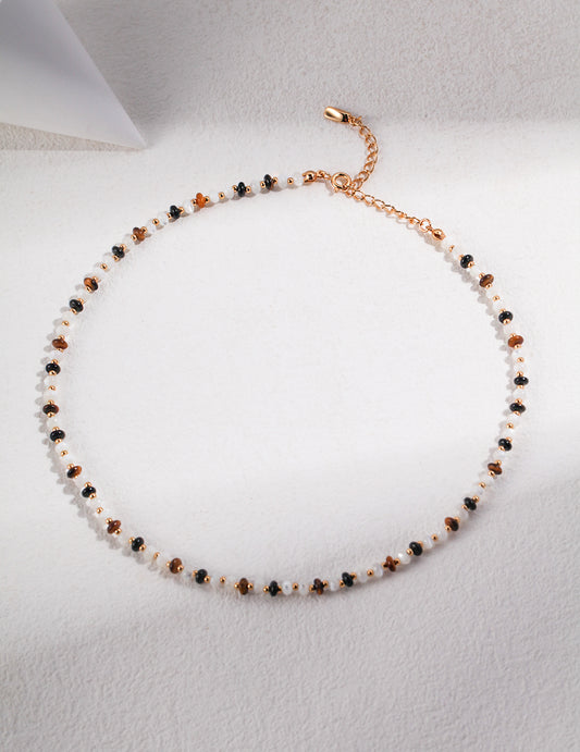 A stunning necklace adorned with gold plated and white silk beads, black agate, and tiger's eye stones.