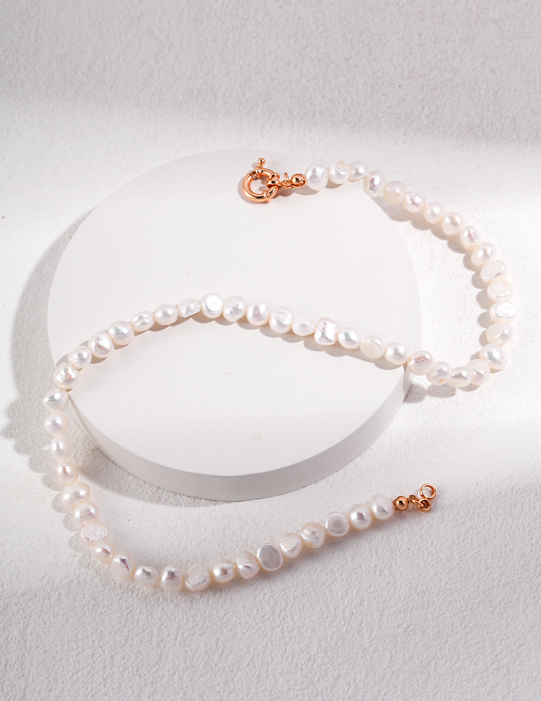 A graceful baroque pearl necklace with a gold clasp, elegantly draped against a soft white backdrop, radiating refined sophistication.