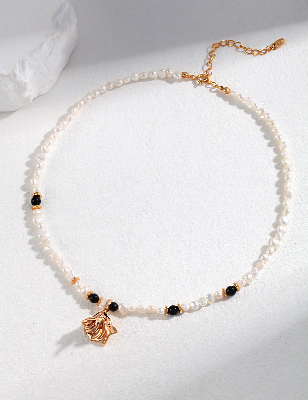 Elegant white pearl necklace with black agate beads and gold charm pendant.