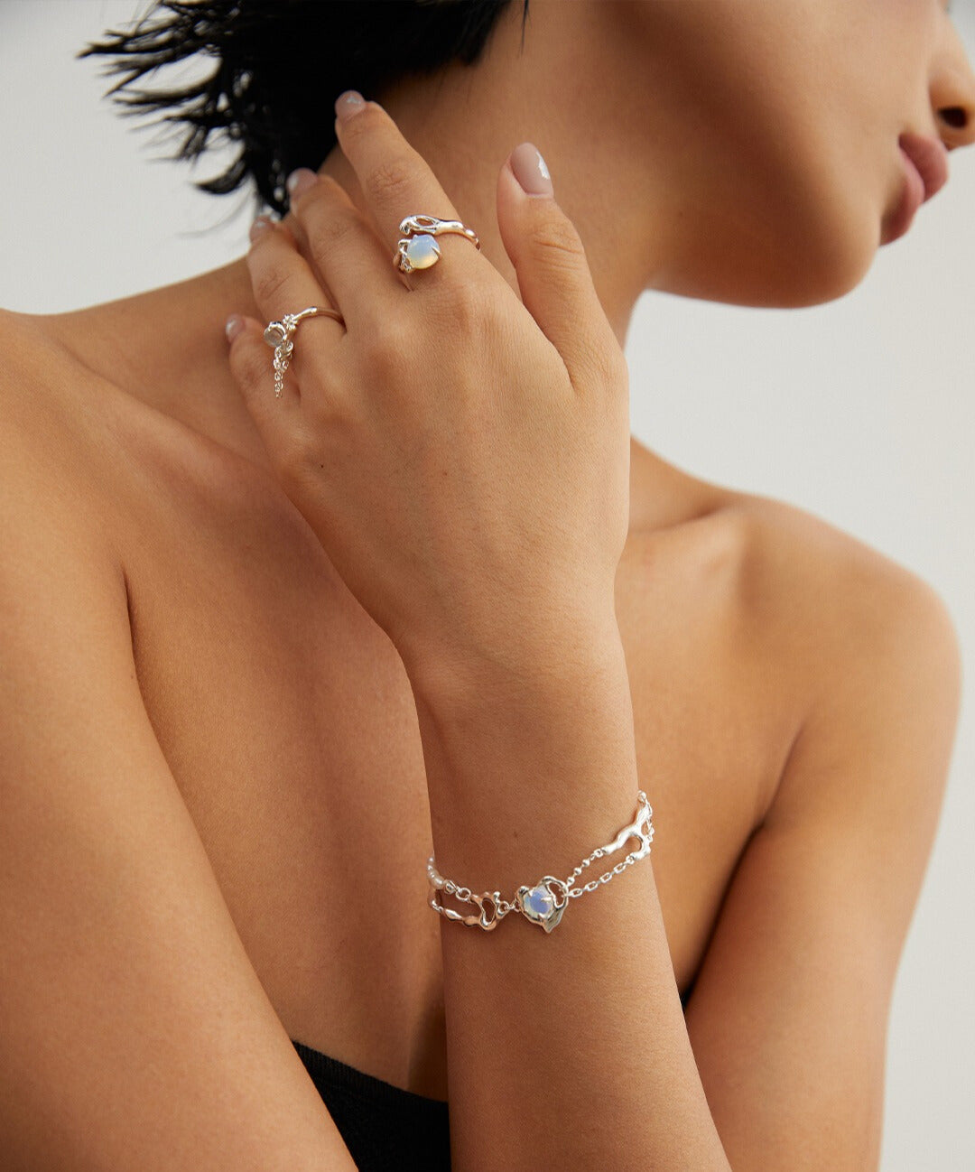 A woman showcasing a silver bracelet, complemented by a stunning silver ring adorned with an opal stone and matching jewelry.