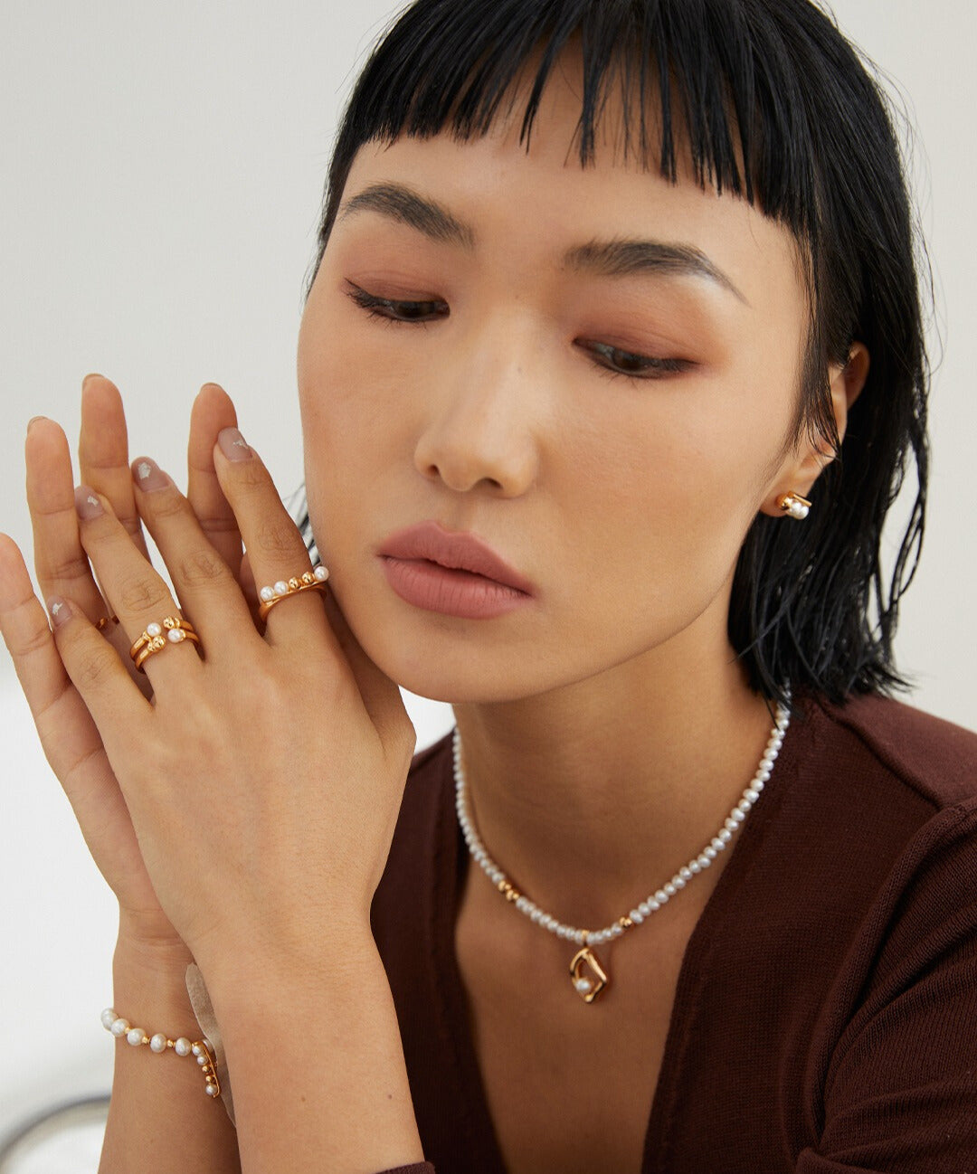 A woman donning a pearl necklace and various gold rings, featuring minimalist styles with shell pearls and beads.