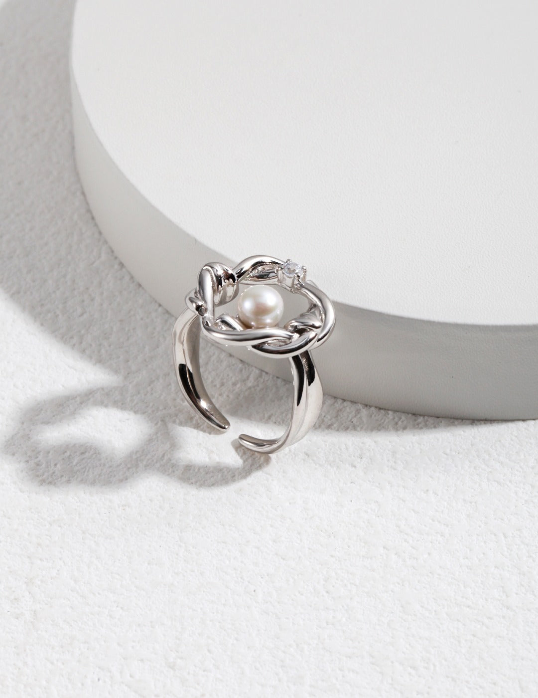 A stunning silver ring adorned with a lustrous pearl and cubic zirconia, featuring a floral design and intricate knot details.