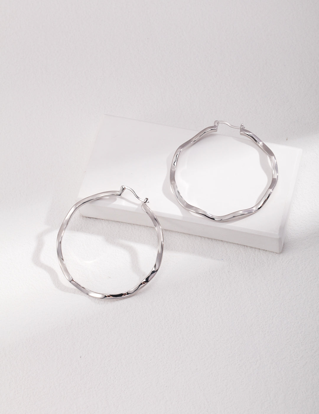 Silver hoop earrings with wavy design on white surface.