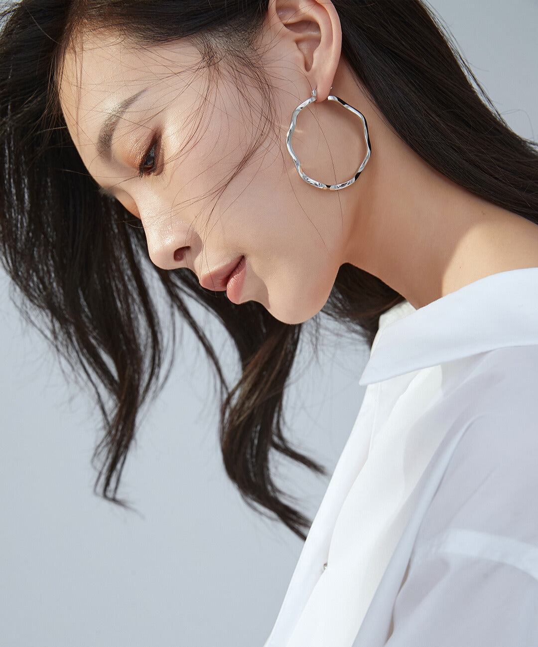 White-shirted woman with silver wavy hoop earrings.