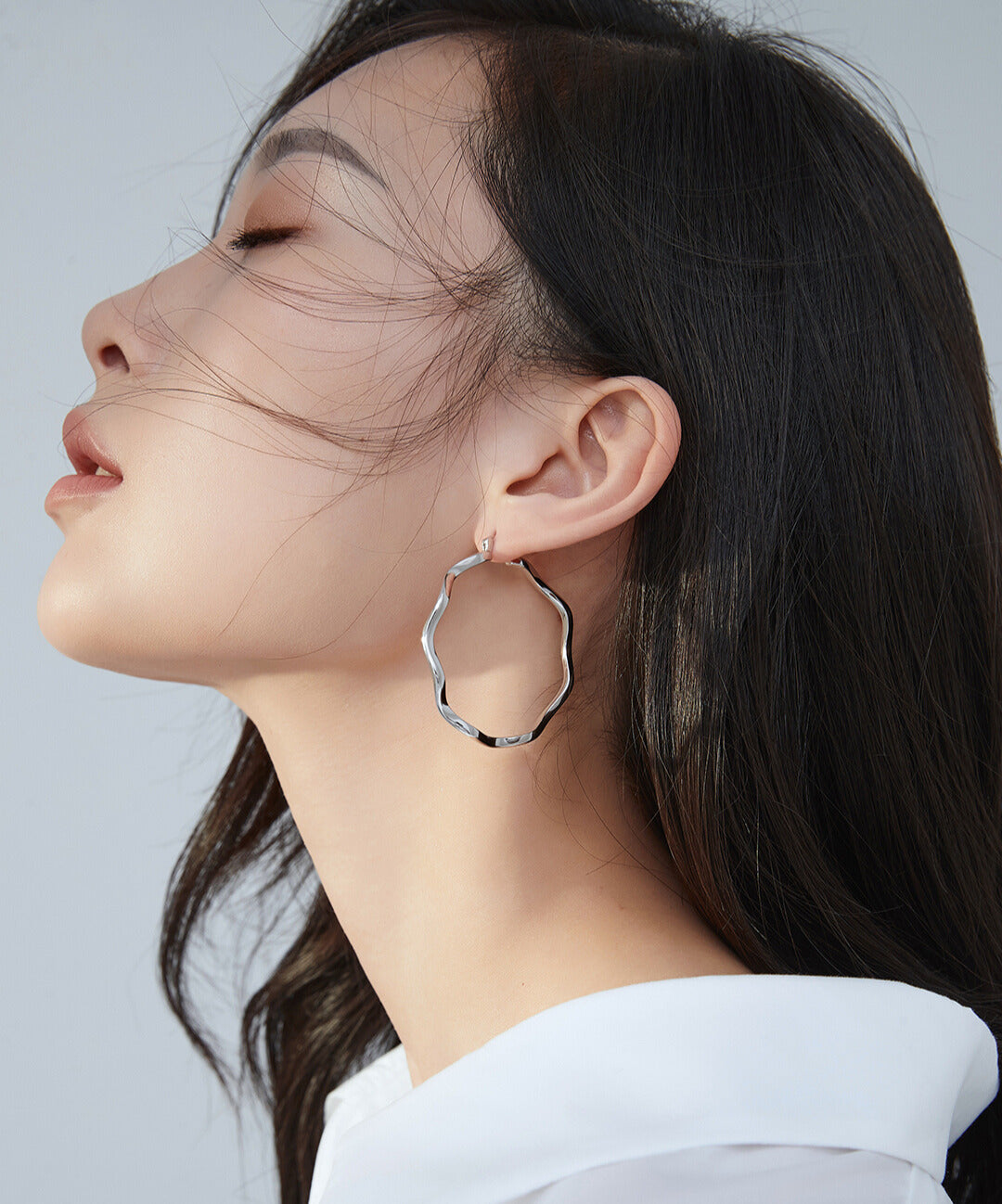 Woman wearing white shirt and silver hoop earrings.