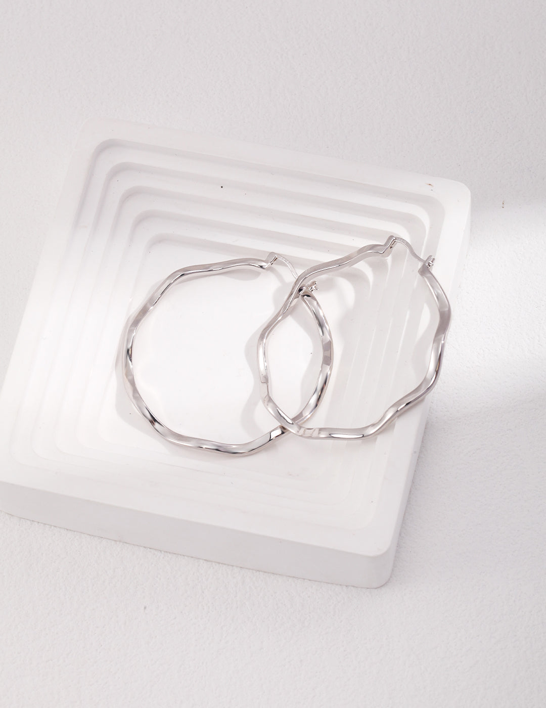 A pair of silver wavey hoop rings on white tray.