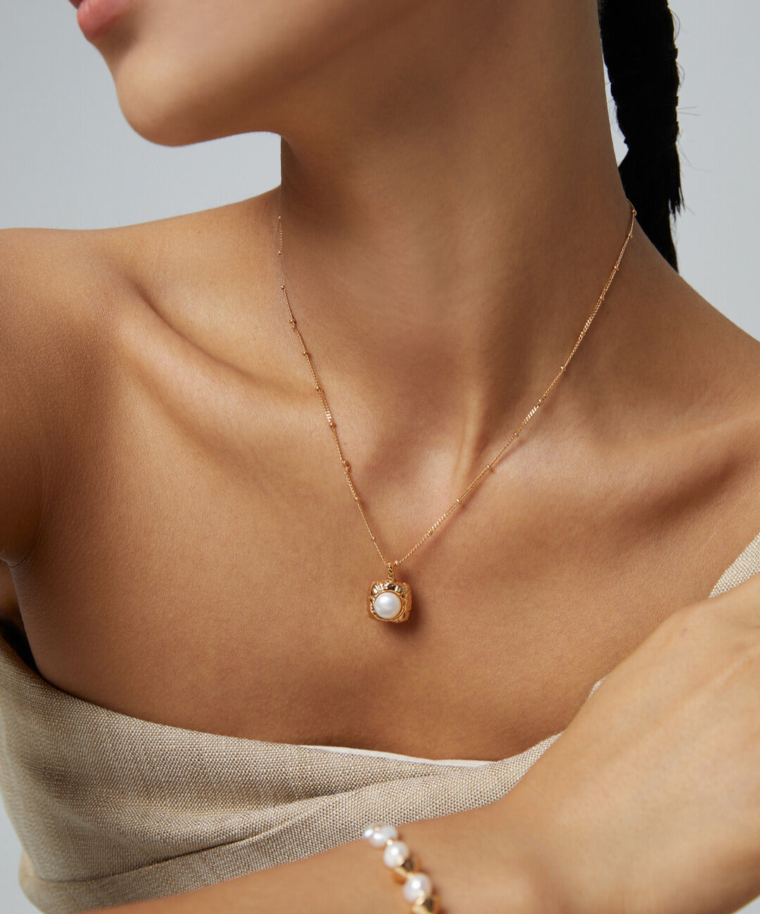 Elegant lady adorned in gold jewelry, including pearl pendant necklace.