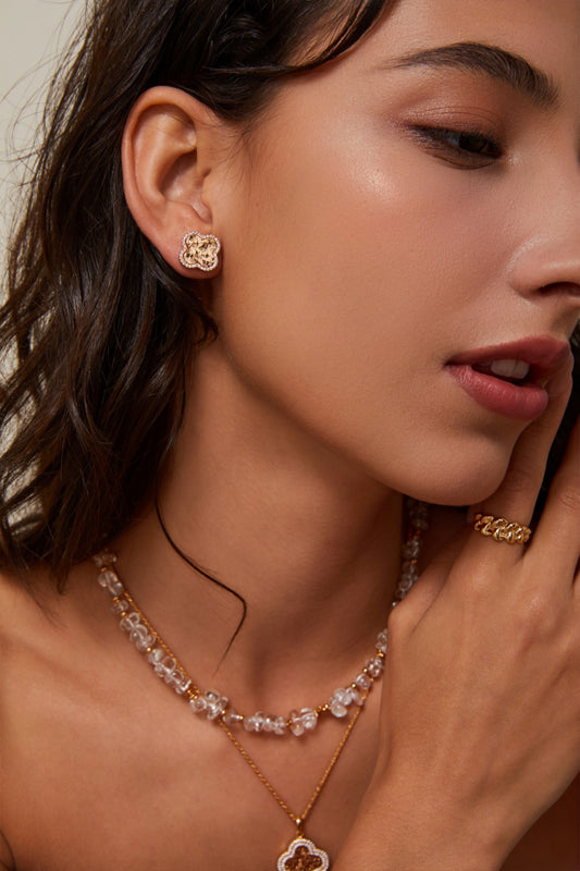 A woman displays a gold necklace and shimmering clover earrings, emphasizing her fashionable accessories.