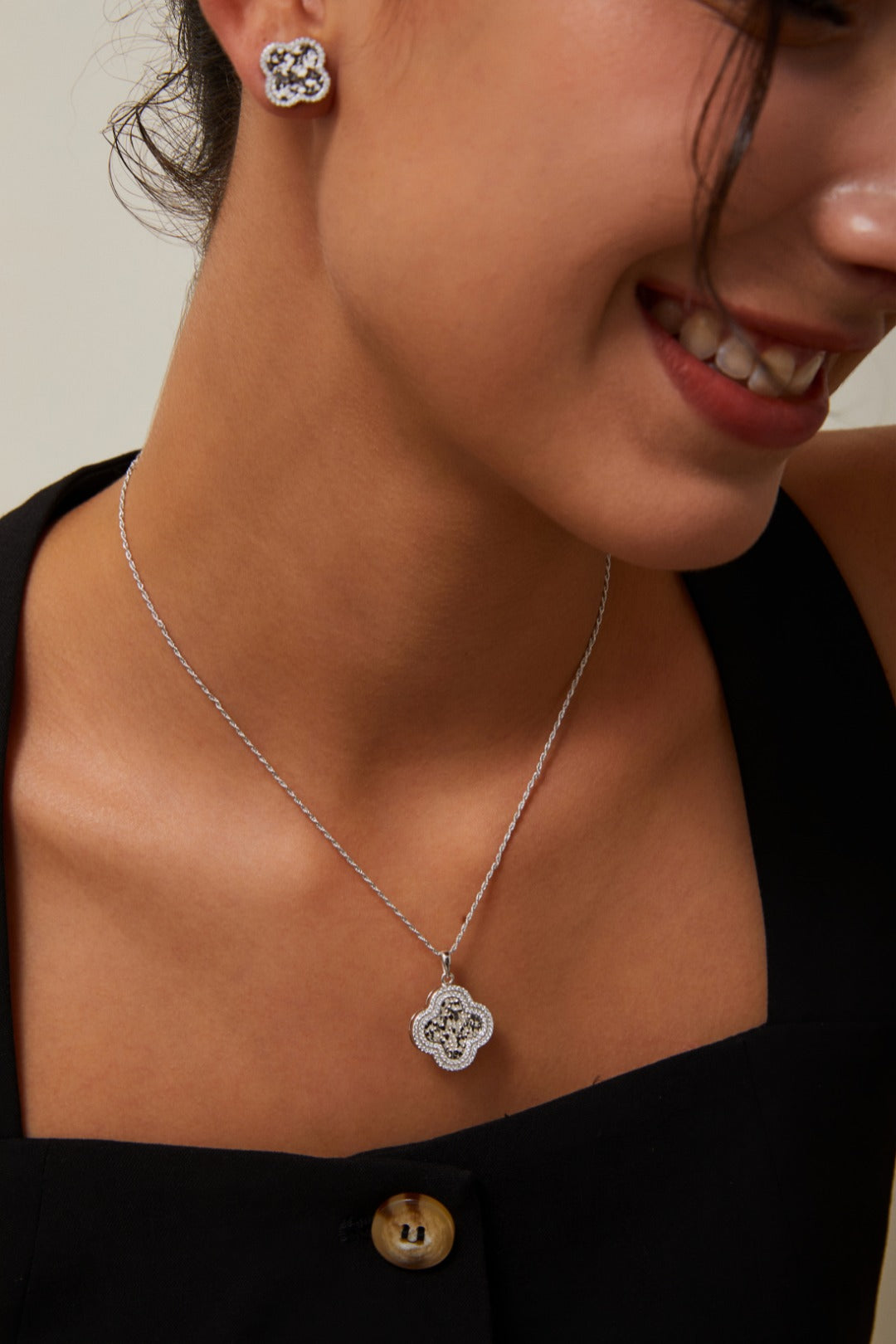 A woman models an elegant clover necklace paired with sparkly silver clover earrings, highlighting her sophisticated and refined style.