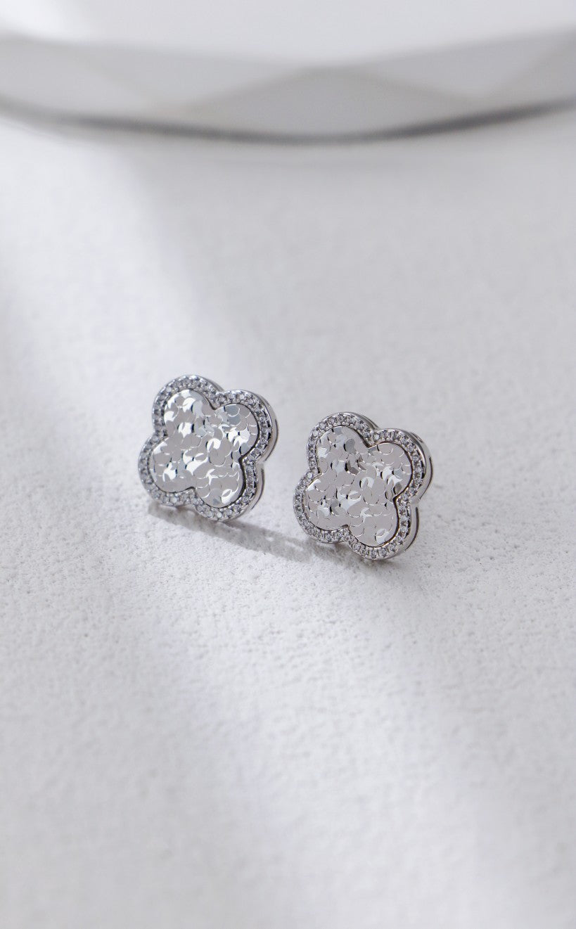 Two small, sparkly silver clover earrings on a white surface, showcasing an elegant and timeless design.