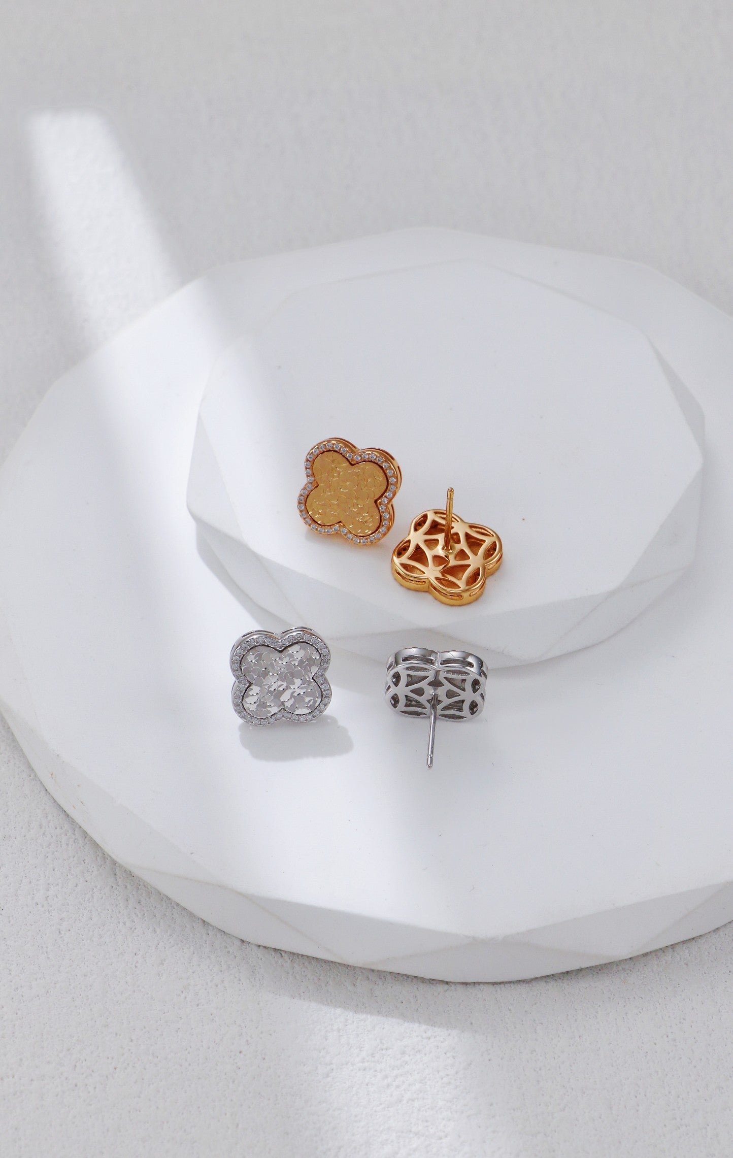 Two clover earrings in silver and gold on a plate, showcasing the intricate designs from both the front and back.