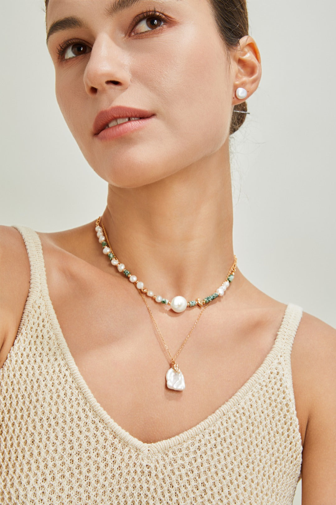 A woman dons a white tank top paired with a stunning pearl petal necklace, radiating sophistication.