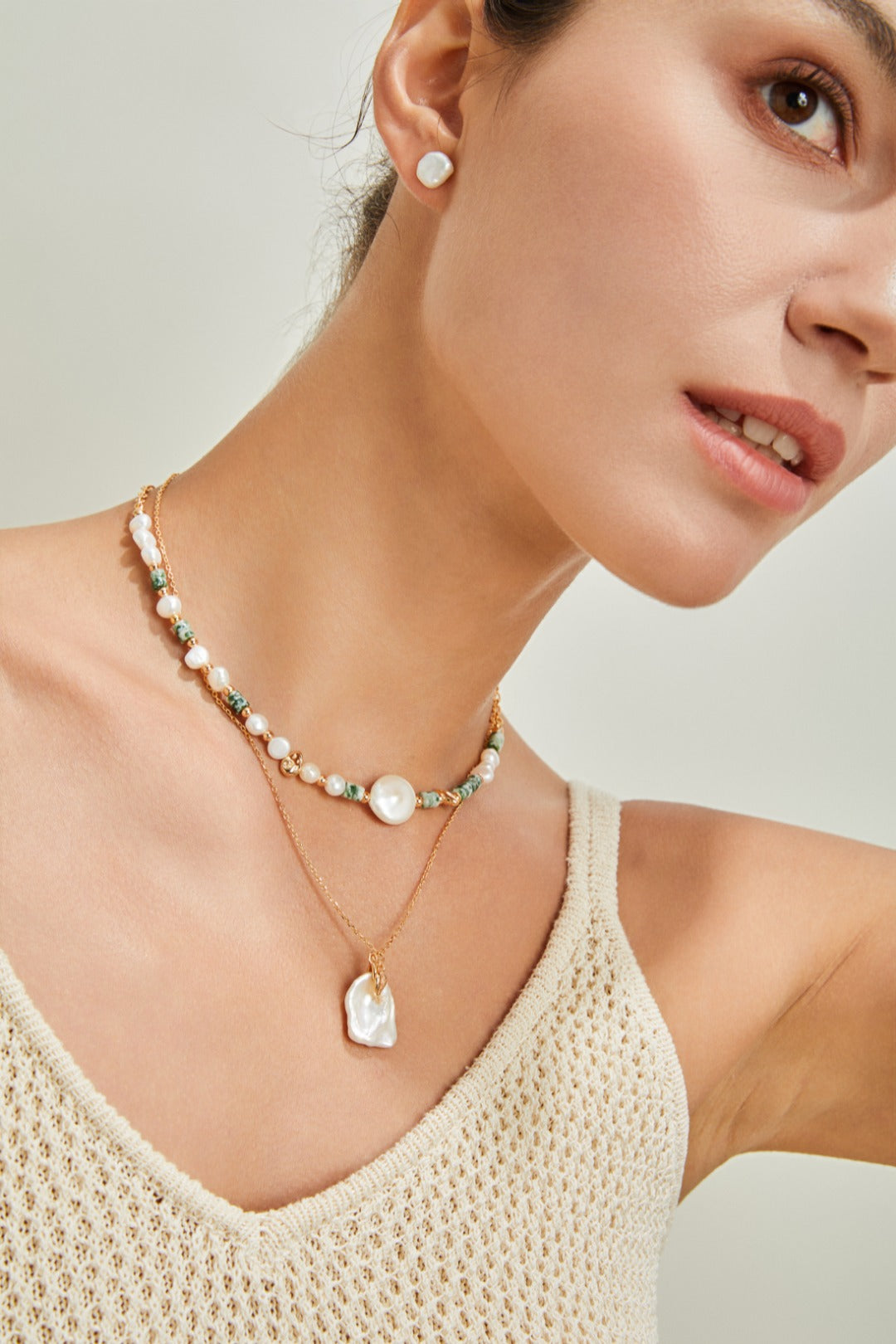 A woman dons a white tank top paired with a stunning pearl petal necklace, radiating sophistication.