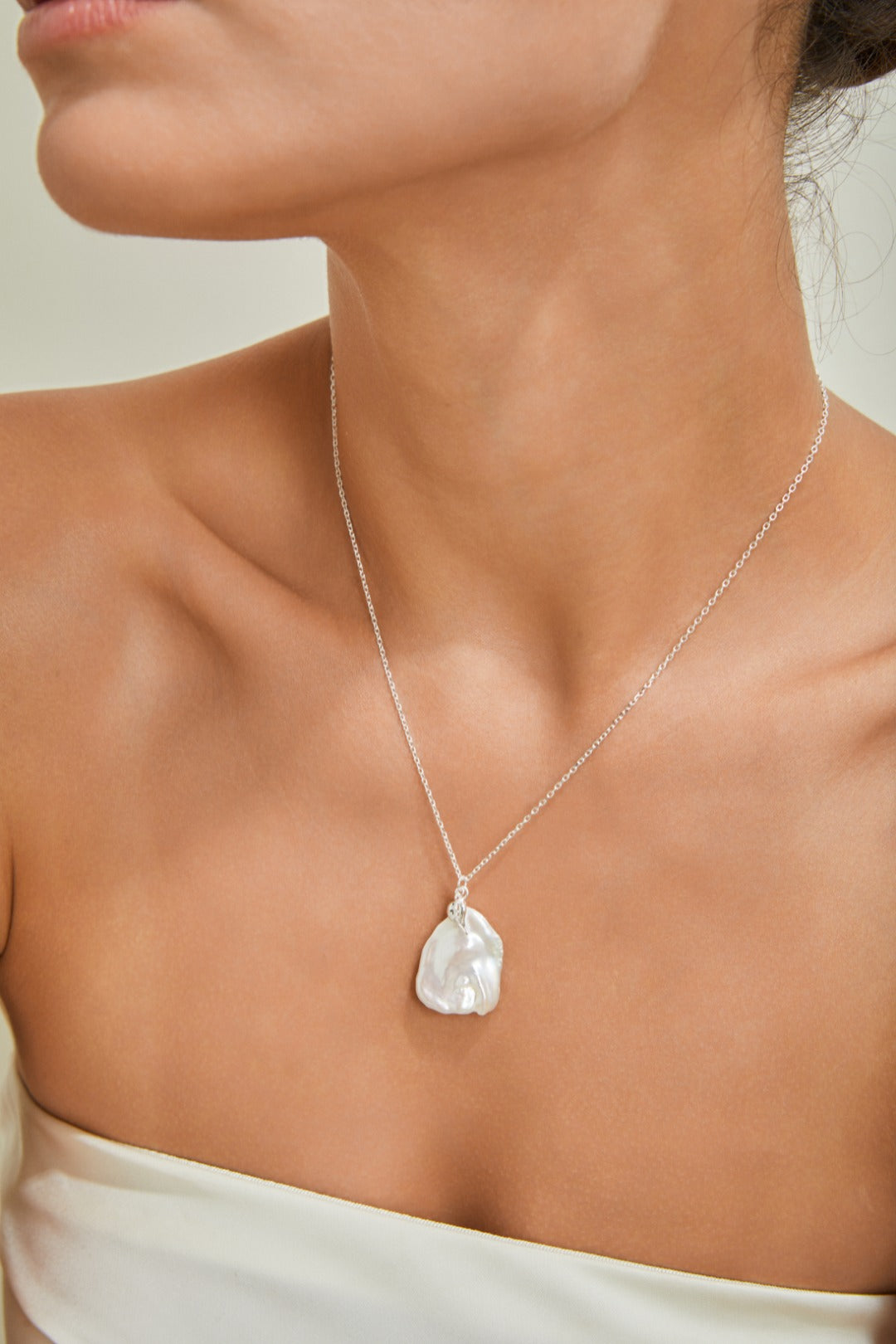 A woman dressed in a white top elegantly wears a silver pearl petal necklace, enhancing her style.